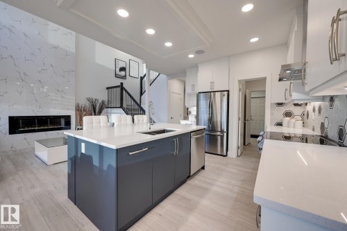 Open-concept kitchen featuring a large island with seating, stainless steel appliances, white cabinetry, and a modern hexagonal tile backsplash - 1776 Crossbill Loop Nw, Edmonton, AB - Indoor Photo Showing Kitchen With Double Sink With Upgraded Kitchen