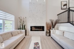 Vaulted ceiling living area featuring a full-height fireplace with stone-finish surround, light wood-finish flooring, and a staircase with dark wood-finish handrail and black balusters - 