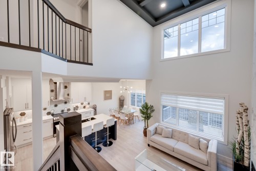 Two-story great room with light wood-finish flooring, a contemporary kitchen featuring a large island, and a dining area - 1776 Crossbill Loop Nw, Edmonton, AB - Indoor Photo Showing Other Room