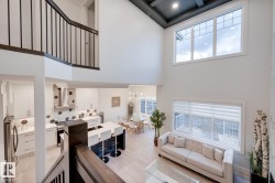 Two-story great room with light wood-finish flooring, a contemporary kitchen featuring a large island, and a dining area - 