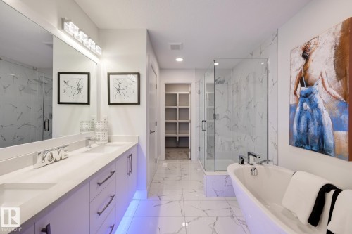 Contemporary bathroom featuring a freestanding tub, glass-enclosed shower, dual vanity with undermount sinks, and a built-in walk-in closet with shelving - 1776 Crossbill Loop Nw, Edmonton, AB - Indoor Photo Showing Bathroom