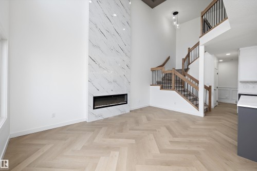 Herringbone wood-finish flooring, a tall fireplace with a marble-look surround, a multi-level staircase with wood railings and black spindles, and a modern pendant light fixture - 1776 Crossbill Loop Nw, Edmonton, AB 