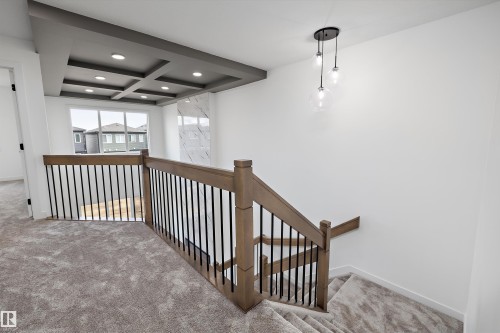 Spacious upper-level landing featuring custom wood-finish railings with metal balusters, recessed ceiling with integrated coffers and pendant lighting, carpet flooring, and abundant natural light from multi-pane windows - 1776 Crossbill Loop Nw, Edmonton, AB 