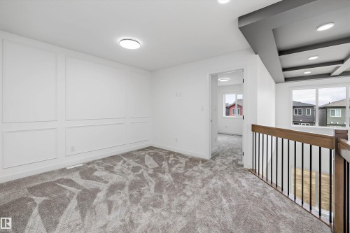 Panel molding accent wall, recessed lighting, neutral tone carpeting, coffered ceiling detail, and wood-finish handrailing with black iron spindles - 1776 Crossbill Loop Nw, Edmonton, AB 