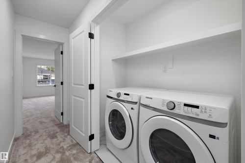 Modern laundry room featuring side-by-side front-load washer and dryer with stainless steel finishes, white shaker-style cabinetry, floating shelving above appliances, and neutral tile flooring throughout - 1776 Crossbill Loop Nw, Edmonton, AB 