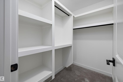 Custom walk-in closet featuring built-in white shelving with multiple compartments, a hanging rod with black hardware, and finished flooring throughout - 1776 Crossbill Loop Nw, Edmonton, AB 