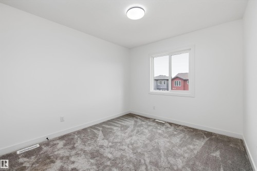 Bright secondary bedroom featuring recessed ceiling lighting, carpet flooring, and a large window with natural light and neighborhood views - 1776 Crossbill Loop Nw, Edmonton, AB 