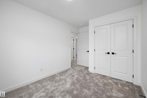 Light-toned textured carpeting, white painted walls, and white paneled doors with black hardware - 1776 Crossbill Loop Nw, Edmonton, AB 