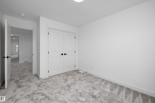 Plush carpet flooring, white painted walls, white paneled bifold closet doors, and matte black hardware - 1776 Crossbill Loop Nw, Edmonton, AB 
