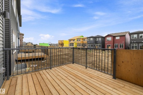 Spacious composite deck featuring warm wood-finish flooring and black metal railing, overlooking a vibrant neighborhood streetscape with colorful residential architecture - 1776 Crossbill Loop Nw, Edmonton, AB 