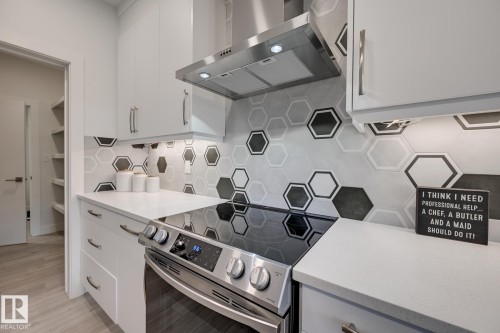 Contemporary kitchen featuring an electric range, stainless steel vent hood, and a unique hexagonal tile backsplash - 1776 Crossbill Loop Nw, Edmonton, AB - Indoor Photo Showing Kitchen