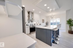Modern kitchen featuring white cabinetry, hexagonal tile backsplash, stainless steel appliances, a center island with a white countertop, and wood-finish flooring - 
