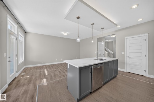 Kitchen island featuring a stainless steel sink, integrated dishwasher, and pendant lighting - 4620 Alwood Way Sw, Edmonton, AB - Indoor Photo Showing Kitchen