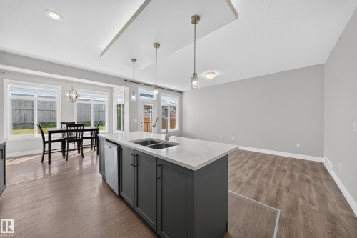 Modern kitchen island featuring a double-basin sink, integrated dishwasher, and pendant lighting - 4620 Alwood Way Sw, Edmonton, AB - Indoor Photo Showing Kitchen With Double Sink