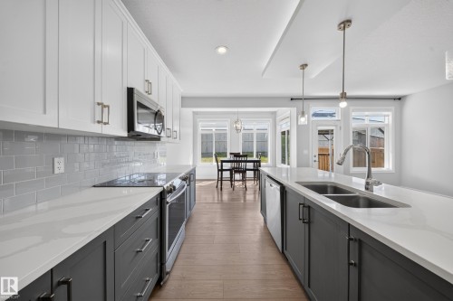 Contemporary kitchen featuring white upper cabinetry, dark lower cabinetry, light countertops, and a subway tile backsplash - 4620 Alwood Way Sw, Edmonton, AB - Indoor Photo Showing Kitchen With Double Sink With Upgraded Kitchen