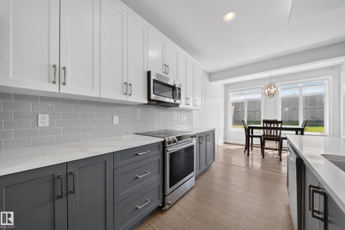 Contemporary kitchen featuring two-tone cabinetry with white upper and gray lower cabinets, quartz countertops, a gray subway tile backsplash, and stainless steel appliances - 4620 Alwood Way Sw, Edmonton, AB - Indoor Photo Showing Kitchen With Upgraded Kitchen