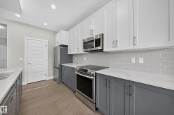 Kitchen featuring two-tone cabinetry with white upper cabinets and gray lower cabinets, stainless steel appliances, a gray subway tile backsplash, white countertops, and wood-finish flooring - 