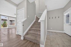 Entry foyer featuring a carpeted staircase with white railings, tile flooring, and a front entry door with a glass insert - 