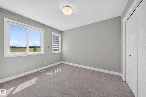 Carpeted room featuring a large window with white trim, a smaller window with blinds, light gray wall paint, and a built-in closet with paneled bifold doors - 4620 Alwood Way Sw, Edmonton, AB - Indoor Photo Showing Other Room