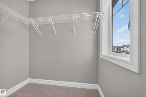 Walk-in closet featuring wire shelving, neutral carpeting, and a casement window with white trim - 4620 Alwood Way Sw, Edmonton, AB - Indoor With Storage