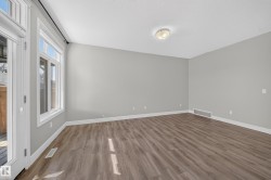 Spacious interior room featuring wood-finish flooring, light gray wall paint, white baseboards, and a white ceiling with a flush-mount light fixture - 