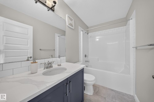 Bathroom featuring a white subway tile backsplash, a dark blue vanity with a light-colored countertop, a white drop-in sink, a standard toilet, and a white bathtub with a shower surround - 4620 Alwood Way Sw, Edmonton, AB - Indoor Photo Showing Bathroom