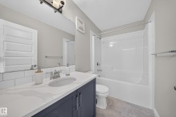Bathroom featuring a white subway tile backsplash, a dark blue vanity with a light-colored countertop, a white drop-in sink, a standard toilet, and a white bathtub with a shower surround - 