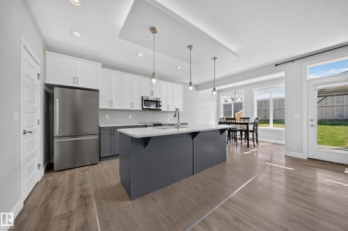 Kitchen featuring a two-tone cabinetry design, central island with pendant lighting, stainless steel appliances, and wood-finish flooring - 4620 Alwood Way Sw, Edmonton, AB - Indoor Photo Showing Kitchen With Stainless Steel Kitchen With Upgraded Kitchen