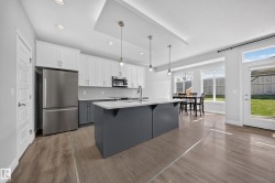 Kitchen featuring a two-tone cabinetry design, central island with pendant lighting, stainless steel appliances, and wood-finish flooring - 