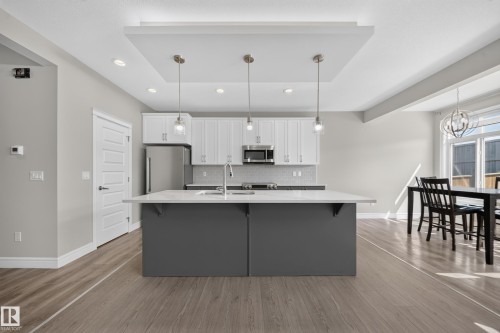 Spacious kitchen featuring a large island with a light-toned countertop, white cabinetry, stainless steel appliances, and a tile backsplash - 4620 Alwood Way Sw, Edmonton, AB - Indoor Photo Showing Kitchen With Double Sink With Upgraded Kitchen