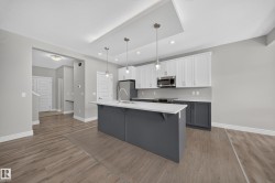 Contemporary kitchen featuring a large island with a white countertop, two-tone cabinetry with white upper and dark gray lower units, stainless steel appliances, and wood-finish flooring - 