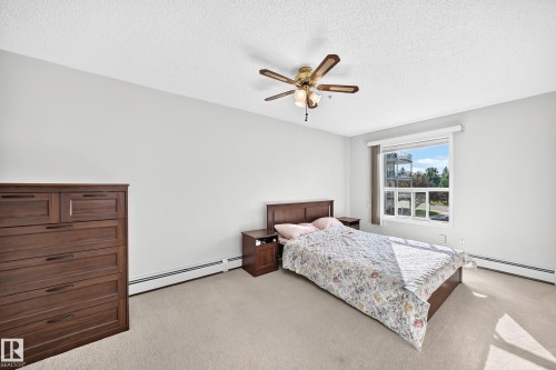 Light-filled room featuring carpet flooring, a window offering exterior views, a ceiling fan with integrated lighting, and baseboard heating - #201 9760 174 St Nw, Edmonton, AB - Indoor Photo Showing Bedroom