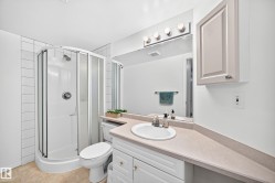 Bathroom featuring a corner shower with glass enclosure, white vanity with integrated sink, light-toned countertop, and mirror with overhead vanity lighting - 