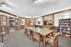 Carpeted common area featuring multiple wood-finish tables and upholstered chairs - 