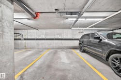 Underground parking space with concrete walls and ceiling, featuring visible utility piping and fluorescent lighting fixtures - 