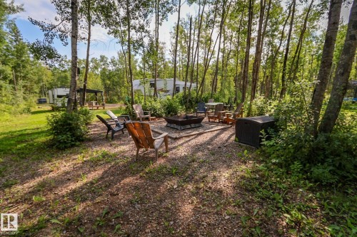 Gravel fire pit area surrounded by mature trees, featuring a metal fire pit and various seating - 200 12272 Township Road 602, Rural Smoky Lake County, AB 