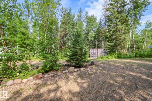 Expansive gravel area surrounded by mature trees, featuring a stone-lined garden bed - 200 12272 Township Road 602, Rural Smoky Lake County, AB 