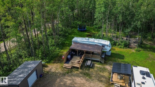 Expansive wooded lot featuring a gravel drive, a shed with a roll-up door, a covered deck with a wooden railing, and established trees - 200 12272 Township Road 602, Rural Smoky Lake County, AB 