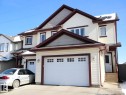Two-story residence featuring light-colored siding with contrasting trim, an attached two-car garage with windowed doors, and a separate side entrance with wood steps - 2153 28 Street Nw, Edmonton, AB  - Outdoor 