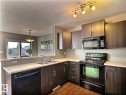 Corner kitchen featuring dark wood-finish cabinetry, black appliances, a double basin stainless steel sink, light-toned countertops, and wood-finish flooring - 2153 28 Street Nw, Edmonton, AB  - Indoor Photo Showing Kitchen With Double Sink 