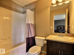 Bathroom featuring a combined tub and shower unit, a dark wood-finish vanity with an integrated sink, a speckled countertop, and a vanity mirror with overhead lighting - 