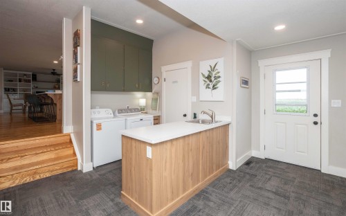 Dedicated laundry area featuring dark green upper cabinetry and a light wood-finish utility island with a stainless steel sink and white countertop - 62503A Hwy 769, Rural Barrhead County, AB - Indoor Photo Showing Laundry Room
