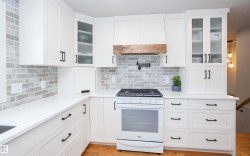 Modern kitchen featuring white cabinetry, light-toned brick-patterned backsplash, white countertops, wood-finish flooring, and a gas range - 