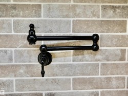 Matte black pot filler faucet with a decorative handle, set against a light-toned brick-patterned backsplash with white grout - 