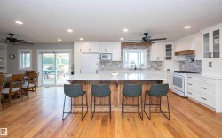Kitchen featuring a wood-finish island with a light-toned countertop, white cabinetry with dark hardware, a light-toned brick-patterned backsplash, and wood-finish flooring - 