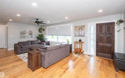 Spacious living area featuring polished wood flooring, recessed lighting, a decorative carved entry door, and a ceiling fan - 