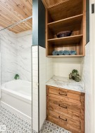 Bathroom featuring a tub with a white marble-patterned surround, wood-finish ceiling, and patterned floor tiling - 