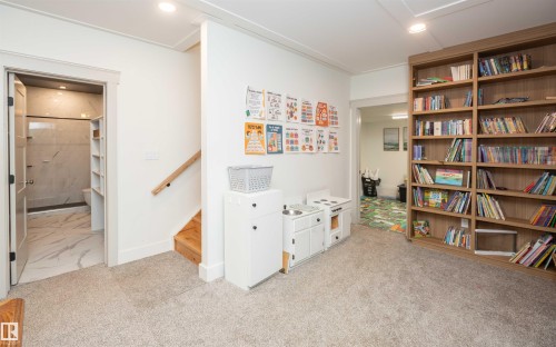 Carpeted room featuring a built-in wood-finish bookshelf, white walls, recessed lighting, and a doorway to a bathroom with marble-finish tile flooring and a walk-in shower - 62503A Hwy 769, Rural Barrhead County, AB - Indoor