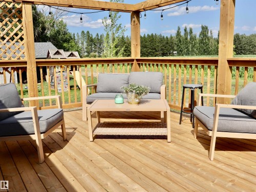 Spacious wood deck featuring a lattice privacy screen, wooden railings, and overhead string lighting - 62503A Hwy 769, Rural Barrhead County, AB - Outdoor With Deck Patio Veranda With Exterior