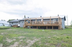 Rear exterior featuring an expansive wood deck with a pergola, a metal roof, and a ground-level patio door - 